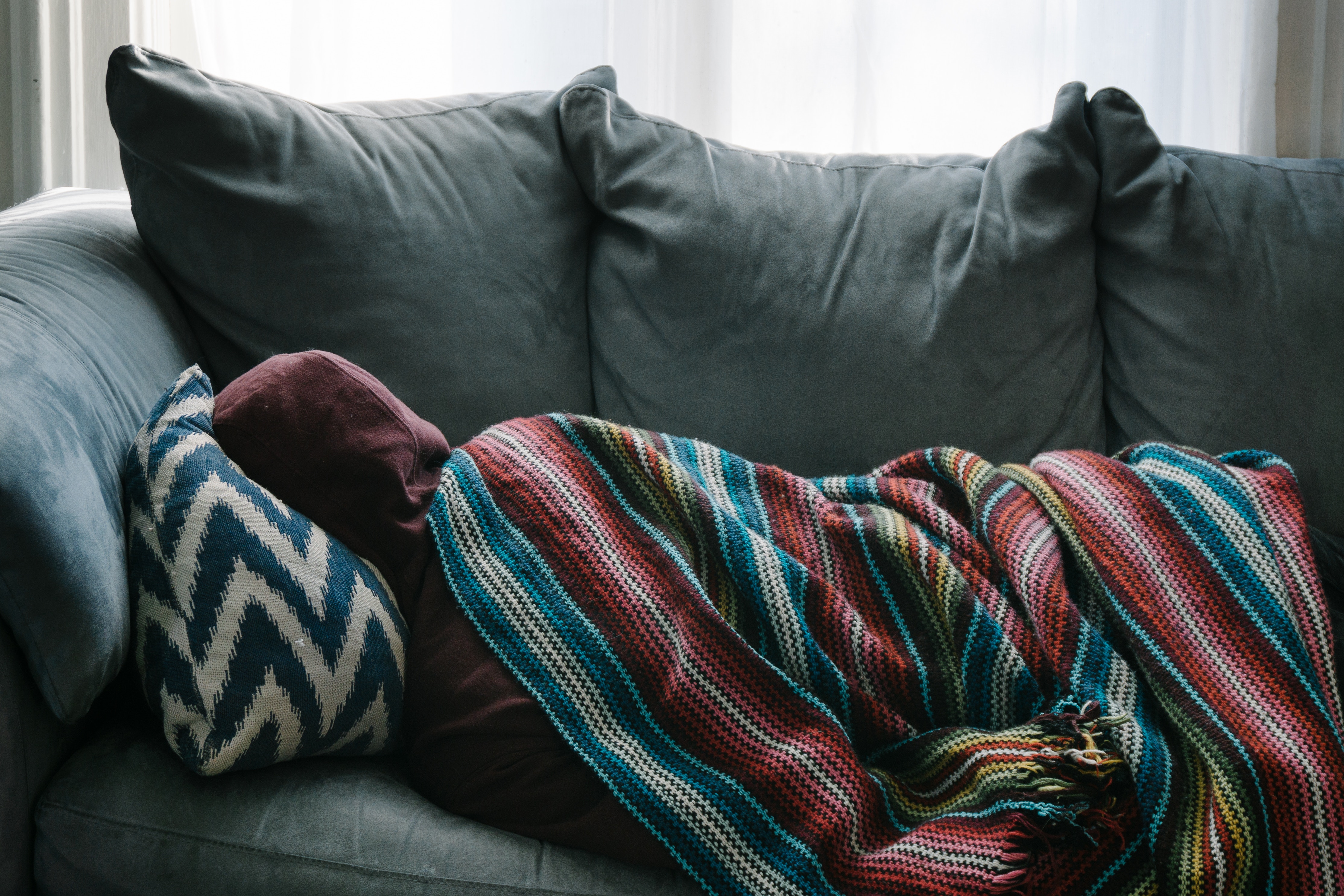 Depression, person sleeping in sofa with a hoodie and blanket